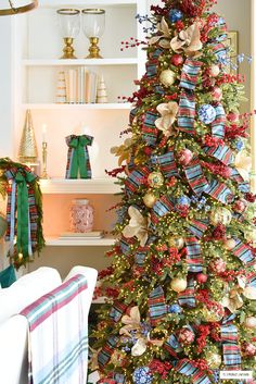 a decorated christmas tree with red, white and blue ribbons on it in a living room