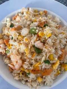 a white bowl filled with rice and shrimp on top of a blue tablecloth covered table