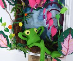 a green stuffed frog sitting on top of a wooden stand next to flowers and leaves