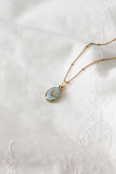 a gold necklace with a small blue stone in the center on a white cloth background