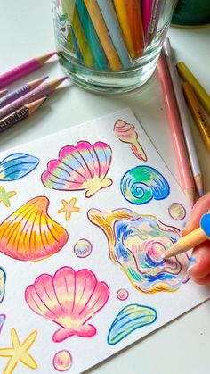 a child's hand is drawing with colored pencils and watercolors on paper