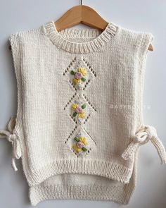 a white sweater with flowers on it hanging from a wooden hanger