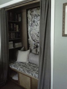 a room with a window seat and bookshelf next to the door that has curtains on it