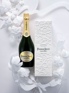 a bottle of champagne sitting next to a box on a white surface with flowers in the background