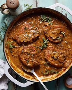 a pot filled with meat covered in gravy and garnished with herbs