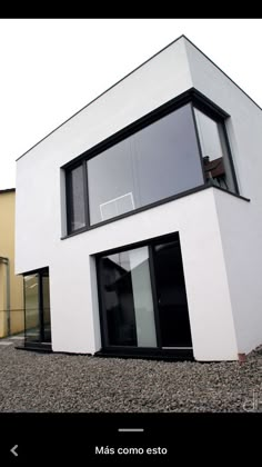 a white house with black trim and windows on the outside, sitting in gravel area next to two buildings