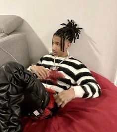 a man with dreadlocks sitting on top of a red bed next to a gray couch