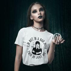 a woman with makeup on her face holding an object in one hand and wearing a t - shirt that says i am not in a bad world, it's just us