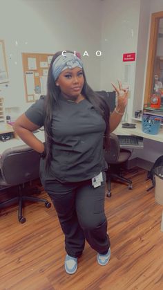 a woman standing in an office wearing scrubs and holding her hand up to the side