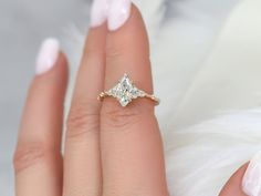 a woman's hand with a diamond ring on top of her finger and white feathers in the background