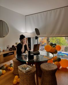 a woman sitting at a glass table with oranges around her