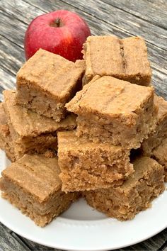 a white plate topped with brownies next to an apple on top of a wooden table