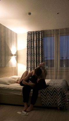 two people sitting on top of a bed in a bedroom next to a window with chevron curtains