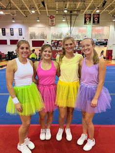 three girls in colorful dresses standing next to each other on a basketball court with people watching from the sidelines