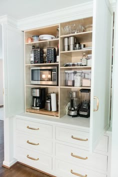 a kitchen with white cabinets and gold handles on the bottom shelf is filled with appliances