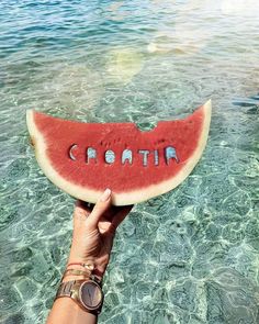 a person holding up a piece of watermelon in the ocean