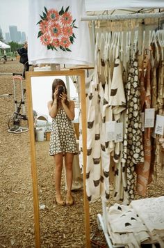 a woman standing in front of a display of clothing on a wooden stand and looking at her cell phone