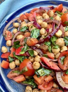 a blue plate topped with lots of veggies and chickpeas on top of lettuce