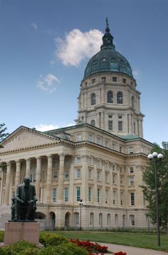 a large building with a statue in front of it and flowers around the perimeter, on a sunny day