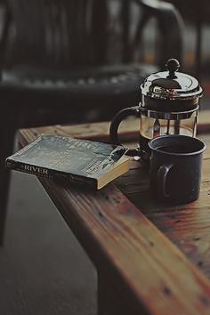 a wooden table topped with a blue coffee cup next to a tea pot and book