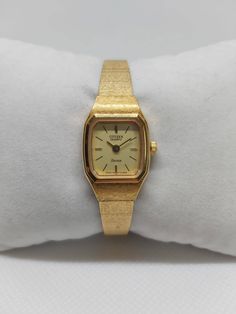 Introducing an impeccably preserved Citizen Seven Ladies Watch, ref. BW-7422-80, purchased in 1984, and still in unworn condition. With its timeless gold-tone stainless steel case and textured bracelet, this beautiful timepiece comes as a full set, including the original box, papers, and receipt from January 26, 1984. The 17mm case width offers a sleek and elegant profile, making it perfect for formal occasions or everyday luxury. Powered by quartz movement, this piece is as reliable as it is st Collectible Gold Watch With Rectangular Dial, Style Année 80, Son Bracelet, Textured Bracelet, Everyday Luxury, January 26, Everyday Luxuries, Women Wrist Watch, Gold Texture