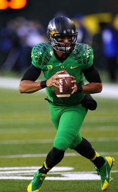 a football player is running with the ball in his hand while wearing green and black