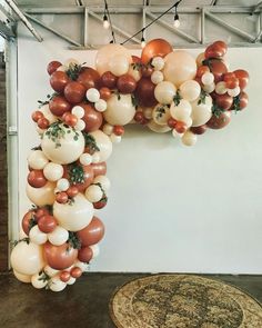 an arch made out of balloons and greenery hangs in the middle of a room