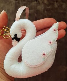 a hand holding a white swan ornament with pink flowers on it's head