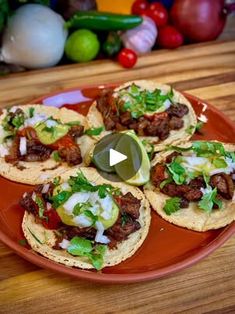 an orange plate topped with tacos covered in meat and veggies on top of a wooden table