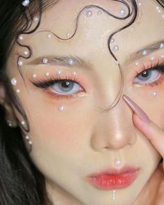 a woman with her face painted in white pearls and holding her hand up to her eye