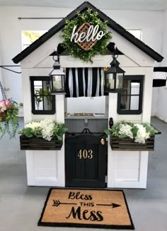 a small house with flowers in the window boxes and welcome mat on the floor next to it