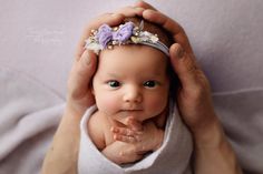 a woman holding a baby in her arms with flowers on it's head and hands