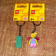 two lego keychains are shown on a brown fabric background, one is yellow and the other is red