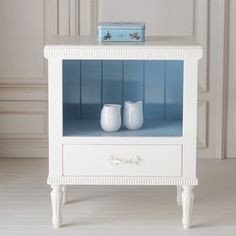 two white vases are sitting on top of a small table with blue walls in the background