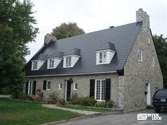 a car is parked in front of a stone house with black shingles and white windows