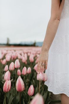 a woman in a white dress is walking through a field of pink tulips