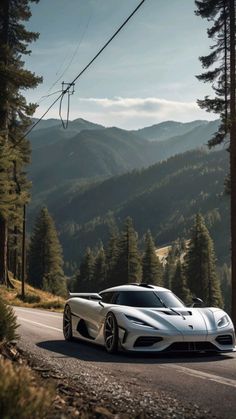 a white sports car driving down the road in front of some trees and mountains on a sunny day