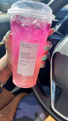 a woman holding up a pink drink in her hand while sitting in the driver's seat