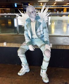 a man sitting on top of a bench covered in white feathers and chains, with his legs spread out