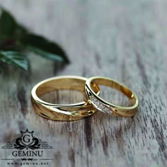 two gold wedding rings sitting on top of a wooden table