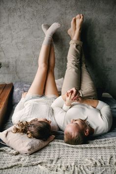 a man and woman laying on top of a bed with their feet up in the air