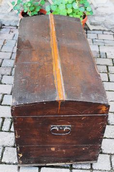 an old wooden trunk sitting on top of a brick sidewalk next to a potted plant