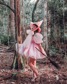 a woman in a pink dress and hat walking through the woods