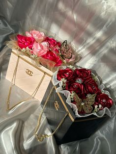 two boxes filled with red roses on top of a silver cloth covered tablecloth and gold chain