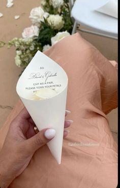 a person holding a paper cone in their left hand with flowers on the table behind them