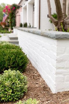 a white brick wall next to some bushes and trees