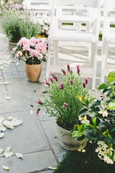 several white chairs sitting on top of a stone floor next to flowers and greenery