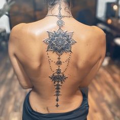 the back of a woman's neck with an intricate tattoo design on her lower back