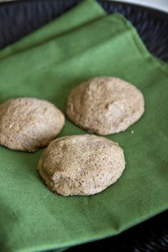 three round cookies sitting on top of a green cloth next to a black plate with two brown ones