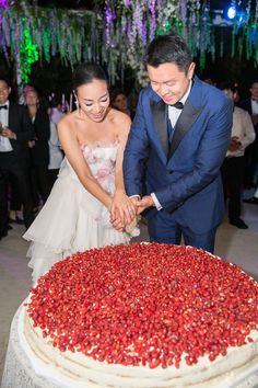 a bride and groom cutting their wedding cake with strawberries on the table in front of them